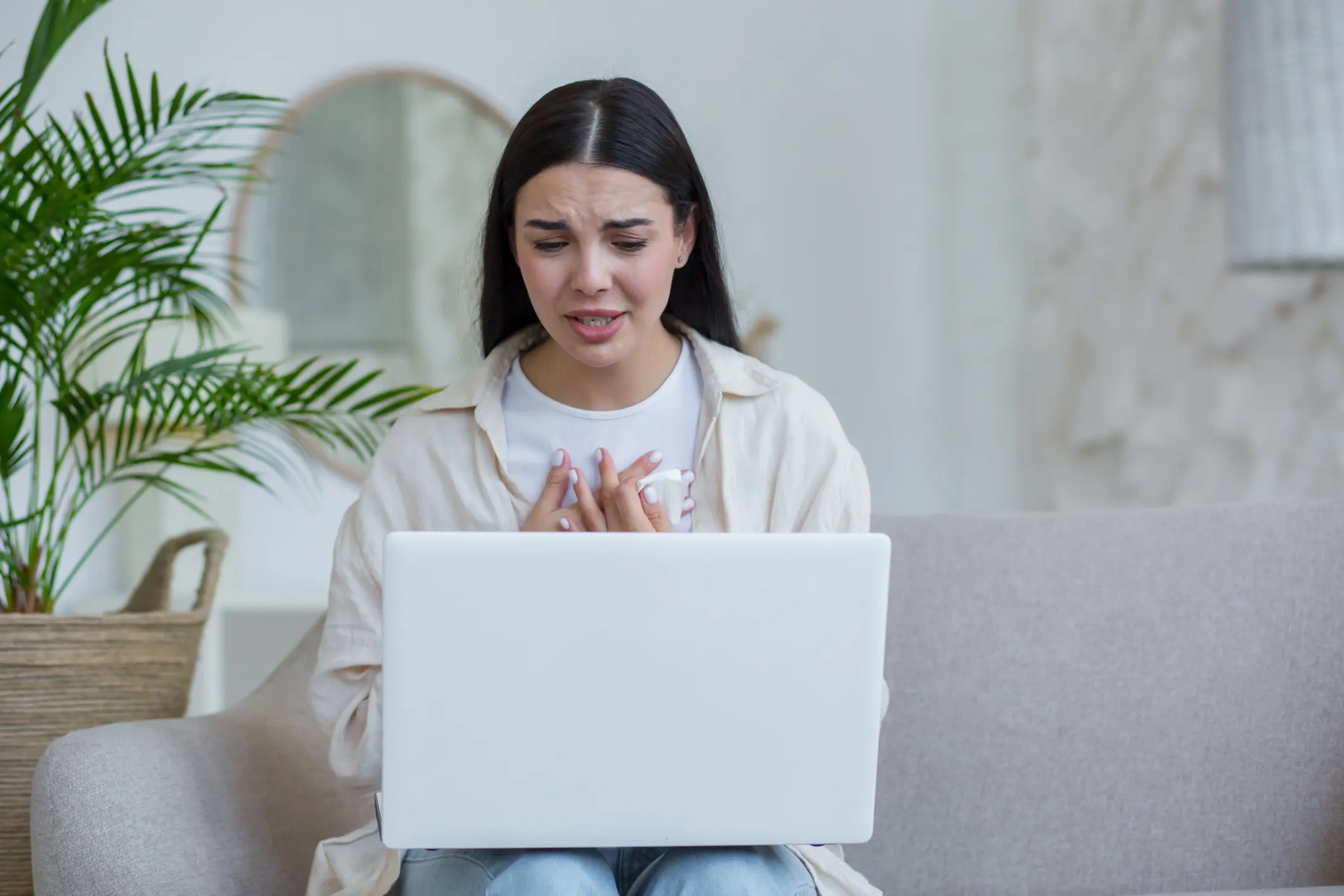 Young beautiful woman alone at home in depression crying, brunette sitting at home and using laptop for online consultation call with psychotherapist