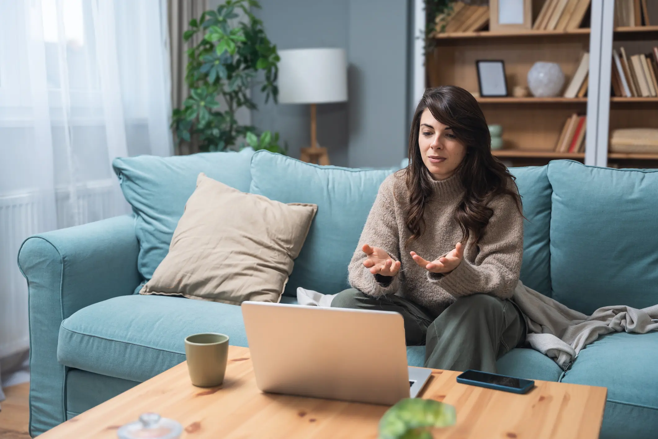 Young woman attending online therapy session from her living room, expressing emotion while talking to a professional therapist, mental health and personal growth support via digital communication.