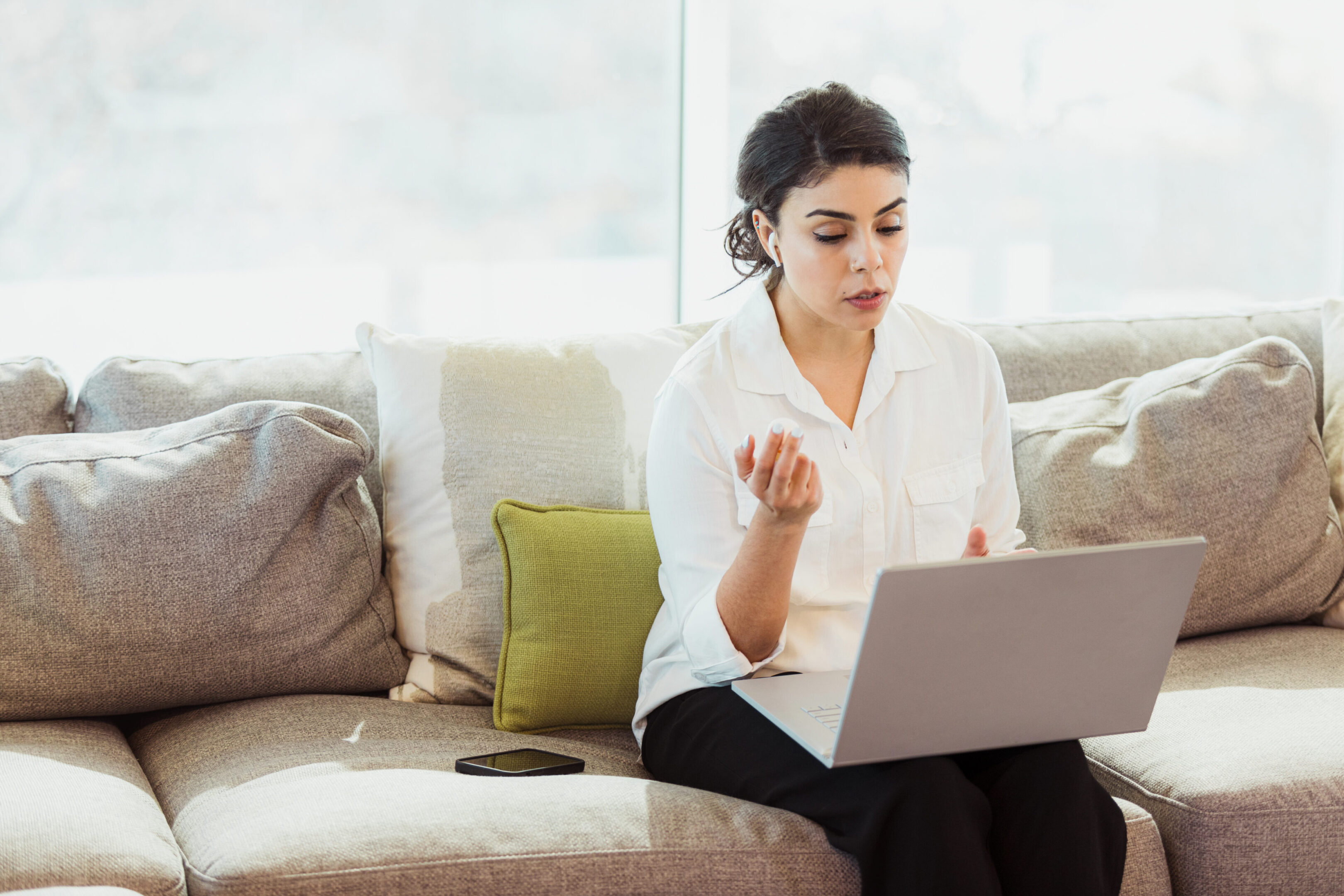 A serious woman holds a pill bottle containing a prescription medication. She is talking to a doctor via telemedicine about the medication's side effects.
