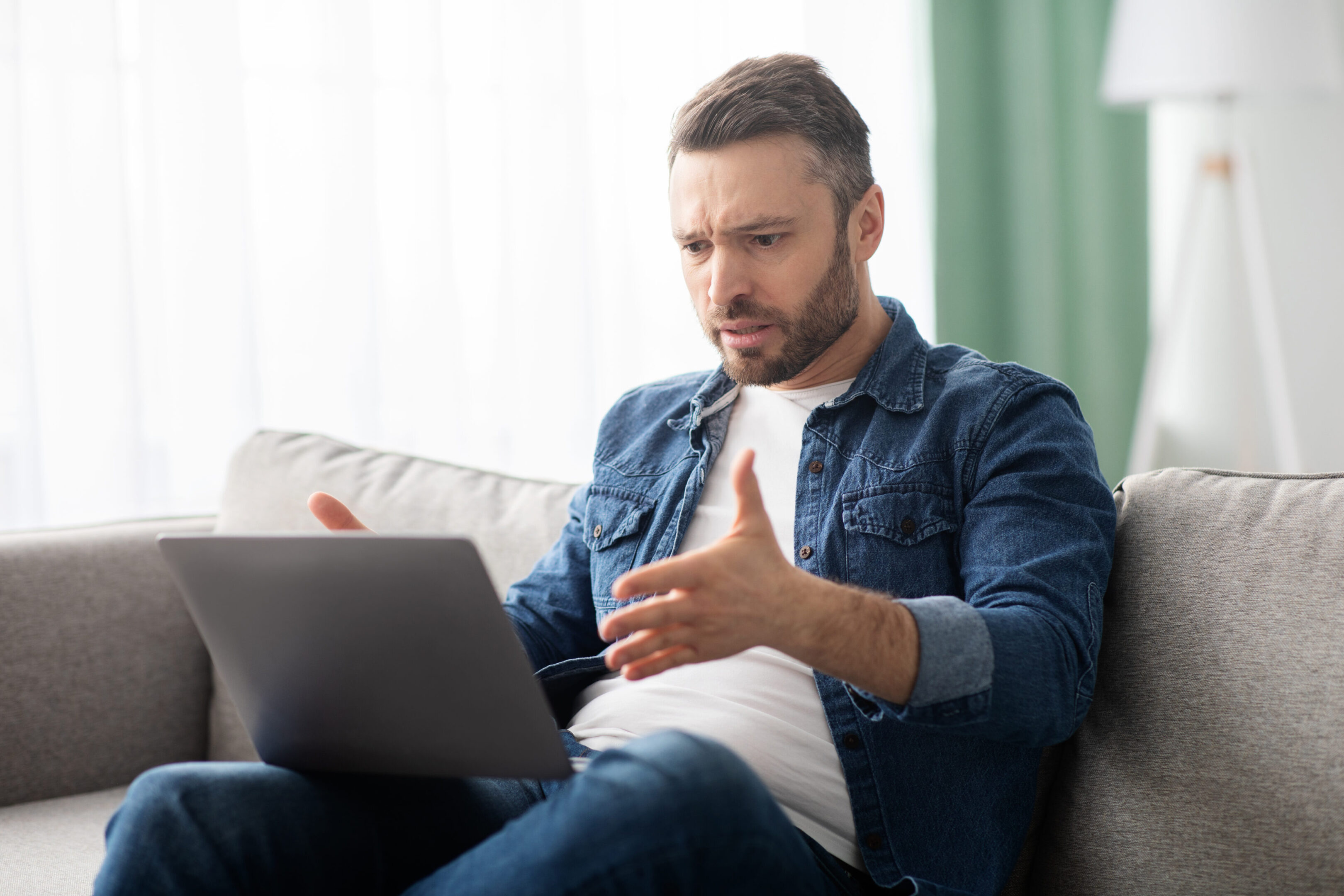 Angry middle-aged bearded man having video call with lover, having fight, using laptop, looking at computer screen, yelling and gesturing, home interior, copy space, side view