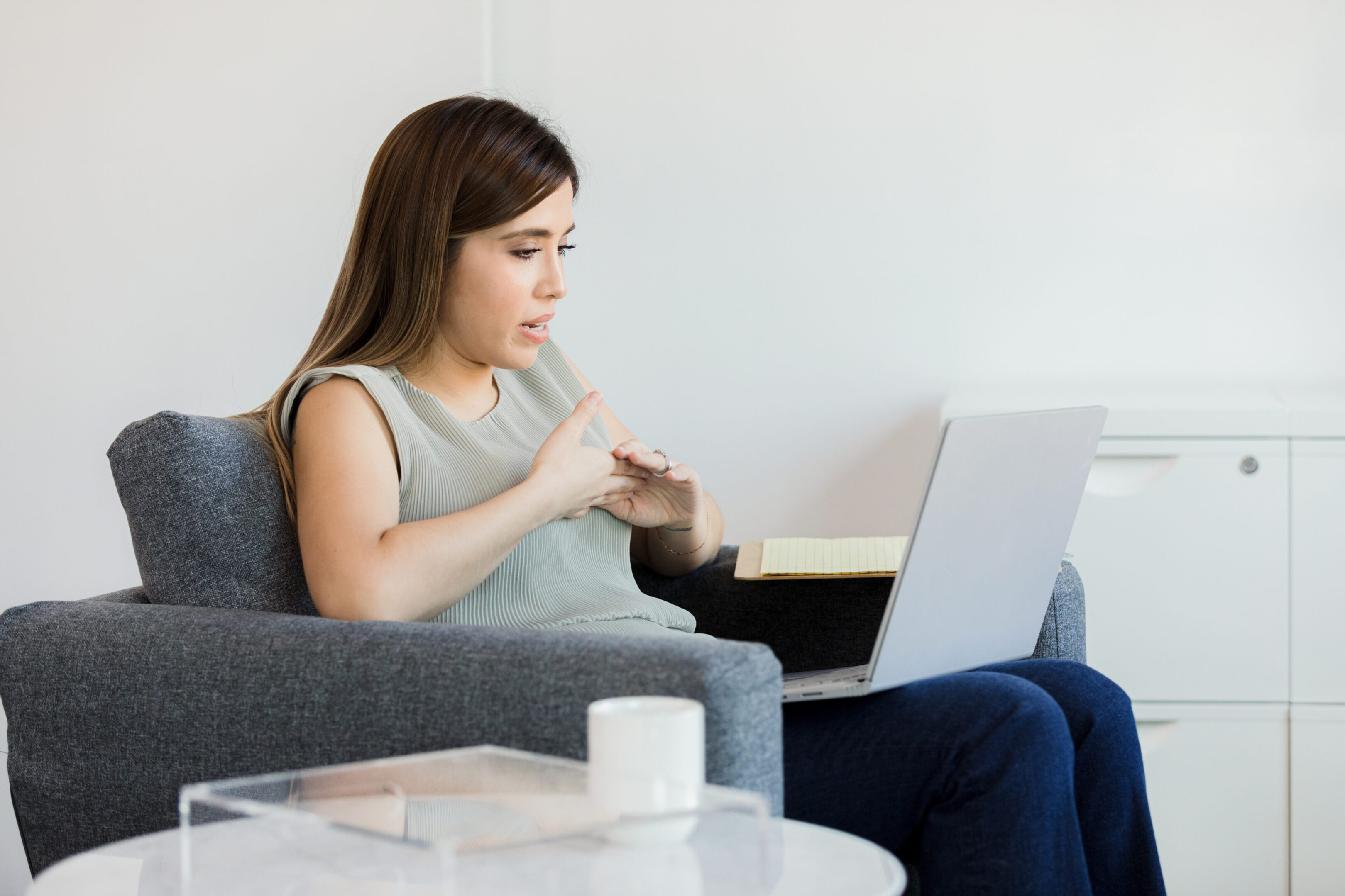 The young adult female psychologist uses her laptop to meet virtually with an unseen patient.